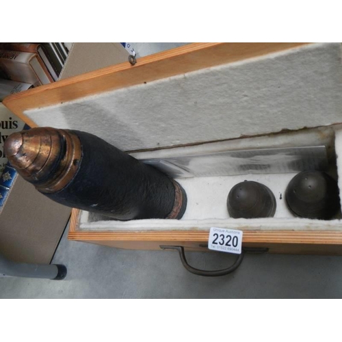 2320 - A wooden box containing a gun shell and three shell heads.