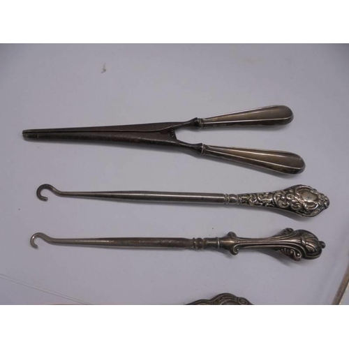 1082 - A mixed lot including silver handles button hooks, silver handled glove stretchers, silver sugar ton... 