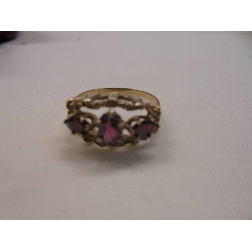 1053 - A three stone ring set with oval garnets in a textured mount gold shank, size P, 2.8 grams.