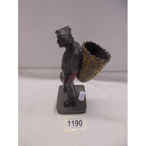 1190 - A painted cast metal figure of a man smoking a cigarette and carrying a basket.