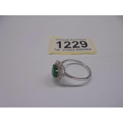 1229 - 18ct white gold ring set with an oval emerald surrounded by RBC diamonds in a scalloped mount. Emera... 