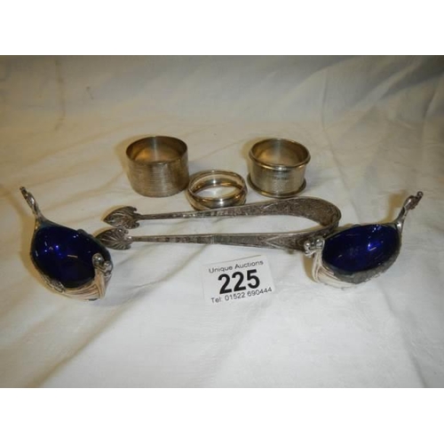 225 - Three silver napkin rings, two plated salts with blue glass linings and a pair of sugar nips.