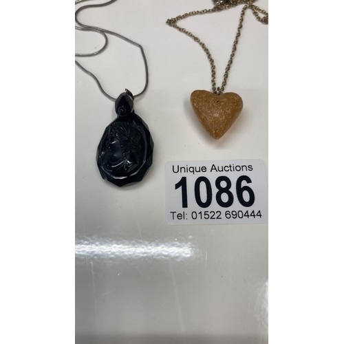 1086 - A Whitby jet pendent of a female profile together with a Amber heart pendant.