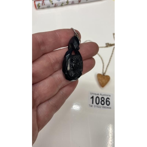 1086 - A Whitby jet pendent of a female profile together with a Amber heart pendant.