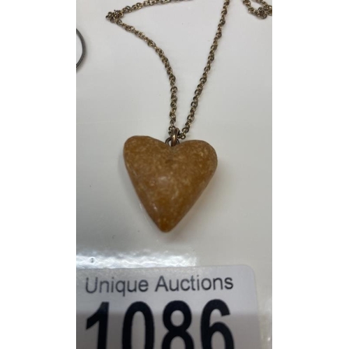 1086 - A Whitby jet pendent of a female profile together with a Amber heart pendant.