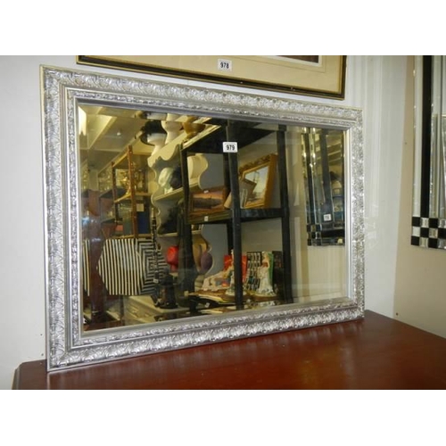 979 - A good bevel edged mirror in a silver coloured frame. COLLECT ONLY.