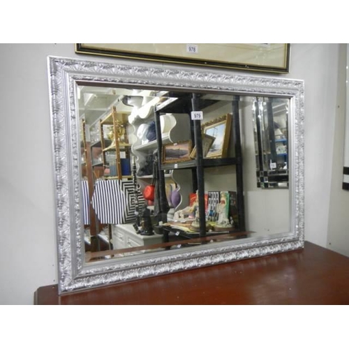 979 - A good bevel edged mirror in a silver coloured frame. COLLECT ONLY.