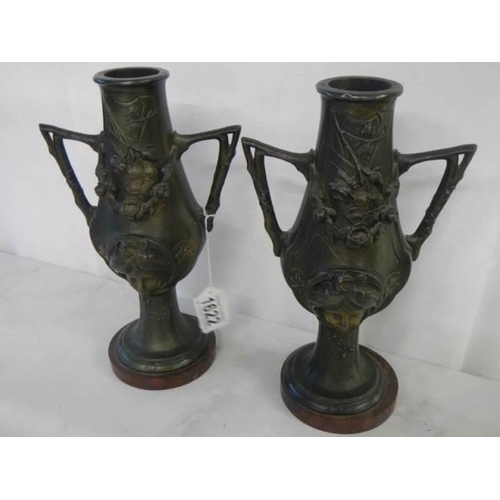 1622 - A pair of bronze vases featuring faces on both sides, 27 cm tall.