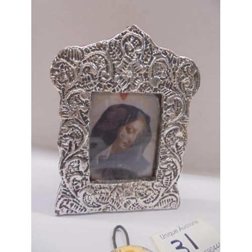 31 - An un-marked silver framed religious print and a metal oval miniature religious plaque.