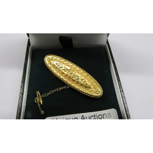 100R - An antique brooch in 15ct hallmarked gold, finely chased gold work with safety chain, 4.5 grams.