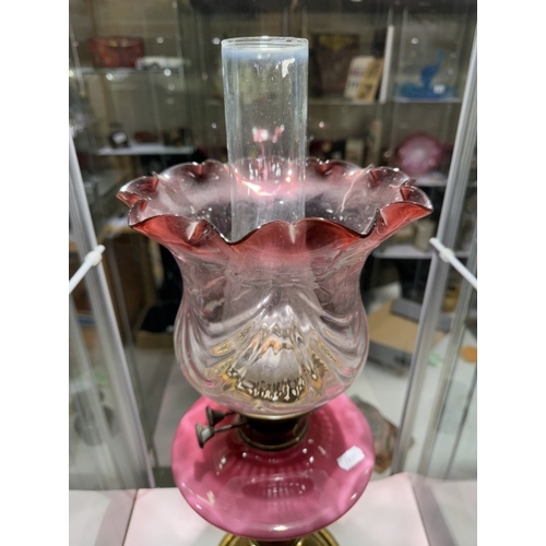 604 - A Victorian oil lamp with brass base, pink art nouveau decorated font on cranberry glass shade