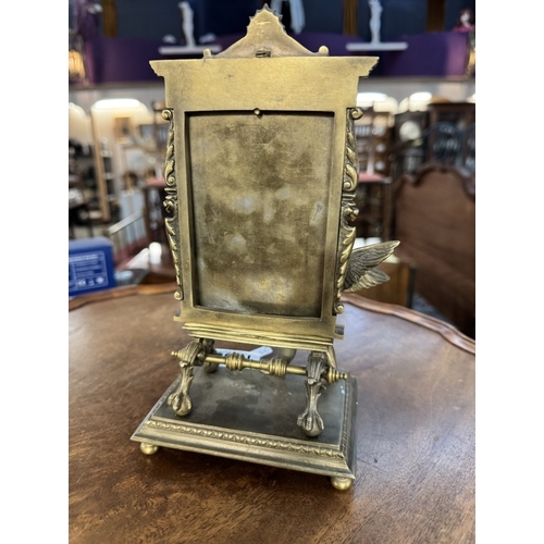 1685 - An ornate brass mirror of a cherub in front of an artists easel, base 12cm x 10cm, height 23cm