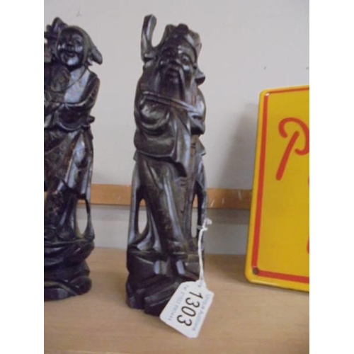 1303 - A pair of carved oriental figures with brass string inlay, 29 cm tall.