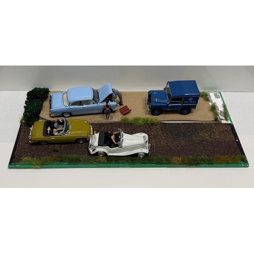 810 - A diorama scene featuring vintage diecast model cars on a gravel & dirt road in acrylic case