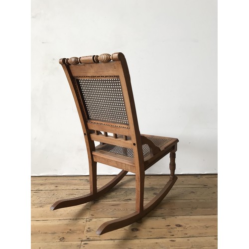 32 - A VICTORIAN MAHOGANY CANE SEATED ROCKING CHAIR, with cane panel back and turned spindle decoration, ... 