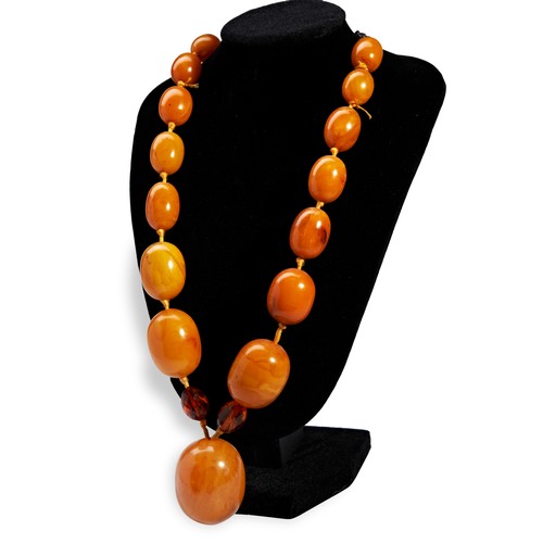 16 - AN AMBER BEAD NECKLACE a single row of graduated amber beads made up of fifteen oval opaque orange y... 