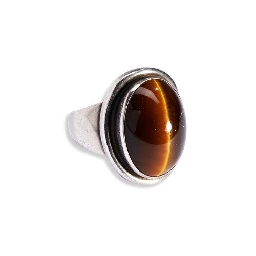 155 - A TIGER'S EYE AND SILVER RING BY GEORG JENSEN the stone set within a collet mount above a silver bor... 