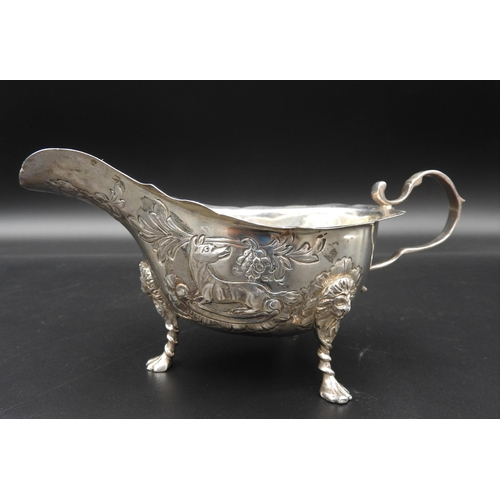 458 - A SILVER SAUCE BOAT WITH REPOUSSE DECORATION, depicting dogs and foliage, on three lion mask paw fee... 