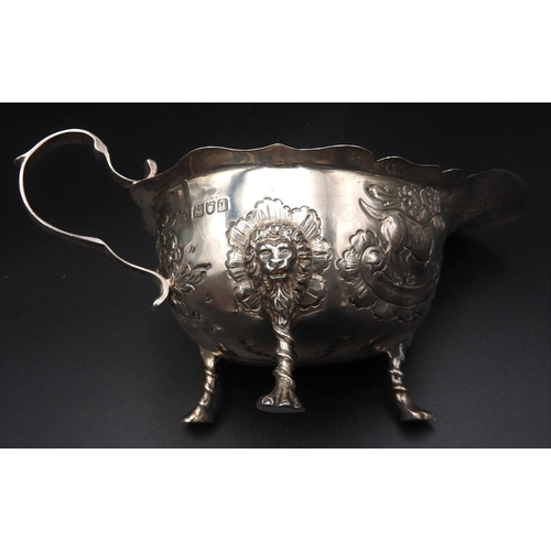 458 - A SILVER SAUCE BOAT WITH REPOUSSE DECORATION, depicting dogs and foliage, on three lion mask paw fee... 