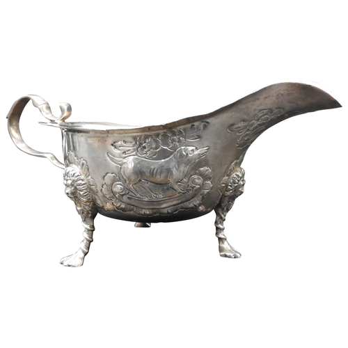 458 - A SILVER SAUCE BOAT WITH REPOUSSE DECORATION, depicting dogs and foliage, on three lion mask paw fee... 