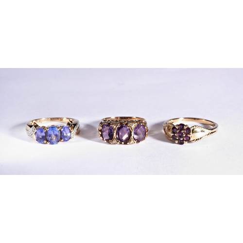 228 - THREE PURPLE STONE DRESS RINGSA three stone blue/purple, claw set, three stone ring with diamond chi... 