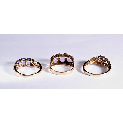 228 - THREE PURPLE STONE DRESS RINGSA three stone blue/purple, claw set, three stone ring with diamond chi... 