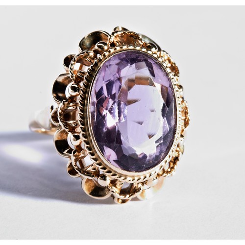 244 - A PURPLE STONE DRESS RINGthe bezel set, mixed cut oval stone, surrounded by rope and wire decoration... 