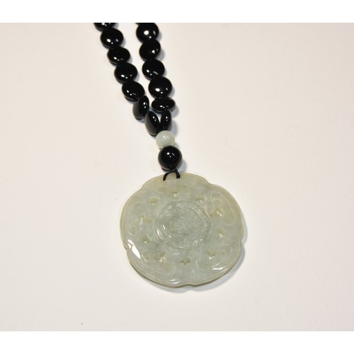 254 - A CARVED JADEITE PENDANT ON AN ONYX BEAD NECKLACE a circular carved jadeite pendant on an onyx bead ... 