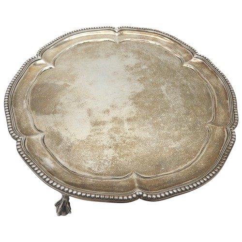 525 - A SMALL SILVER SALVER, with a beaded scroll work edge, raised on three claw and ball feet, bears the... 