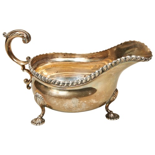 528 - A SILVER SAUCE BOAT, with ornate scroll foliate handle, gadrooned edge, raised on three shell form f... 