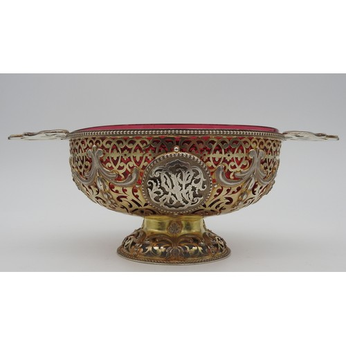 291 - AN UNUSUAL SILVER GILT OVAL BOWL, with cranberry glass liner, pierced scroll work sides emblazoned w... 