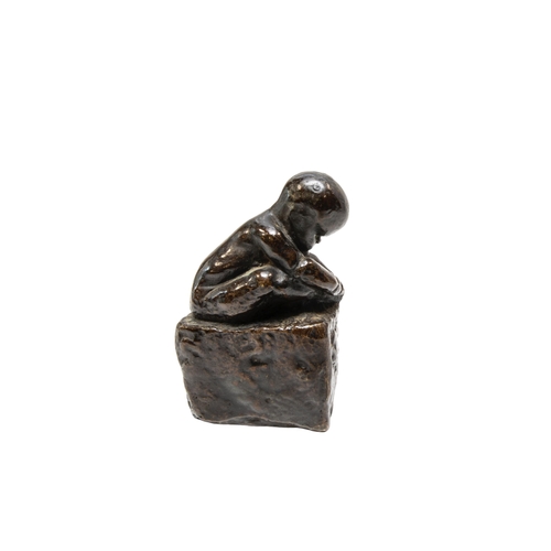 265 - A CAST BRONZE FIGURE OF A CROUCHING INFANT, modelled holding his foot, sat atop a rectangular plinth... 