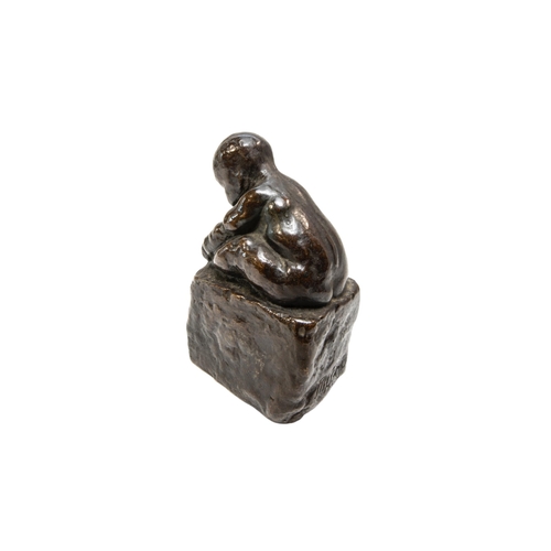 265 - A CAST BRONZE FIGURE OF A CROUCHING INFANT, modelled holding his foot, sat atop a rectangular plinth... 