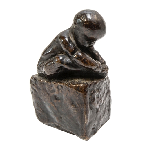 265 - A CAST BRONZE FIGURE OF A CROUCHING INFANT, modelled holding his foot, sat atop a rectangular plinth... 