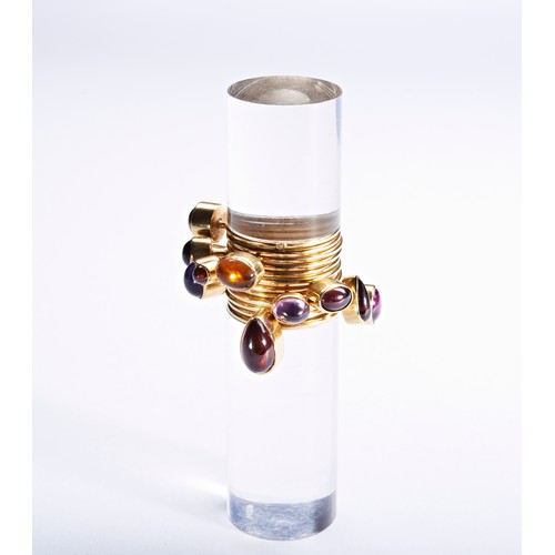 319 - WENDY RAMSHAW; AN AMETHYST, GARNET, AND GOLD RING ON AN ACRYLIC STANDthe ring composed of twelve ban... 