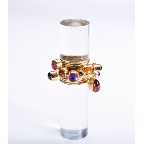 319 - WENDY RAMSHAW; AN AMETHYST, GARNET, AND GOLD RING ON AN ACRYLIC STANDthe ring composed of twelve ban... 