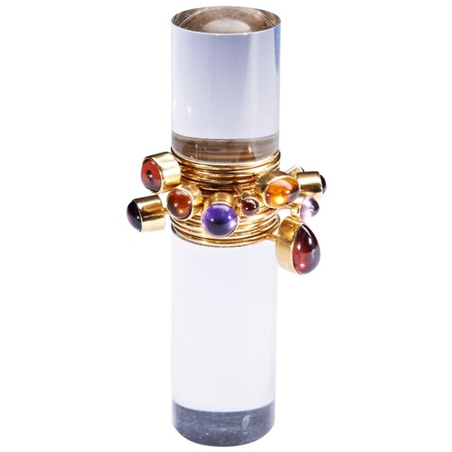 319 - WENDY RAMSHAW; AN AMETHYST, GARNET, AND GOLD RING ON AN ACRYLIC STANDthe ring composed of twelve ban... 