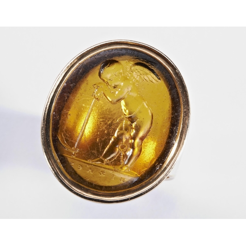 218 - AN NINETEENTH CENTURY GLASS AND GOLD SEAL RINGthe oval glass plaque depicting a winged putti within ... 