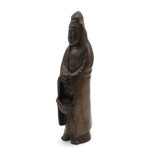 415 - A BRONZE FIGURE OF GUAN YIN, 20TH CENTURY, modelled standing in flowing robes holding a basket with ... 