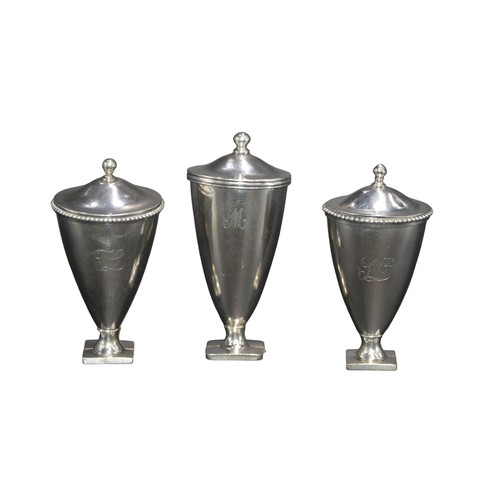 810 - A GROUP OF THREE UNUSUAL WHITE METAL NUTMEG GRATERS, modelled as tapering urns with domed covers, th... 