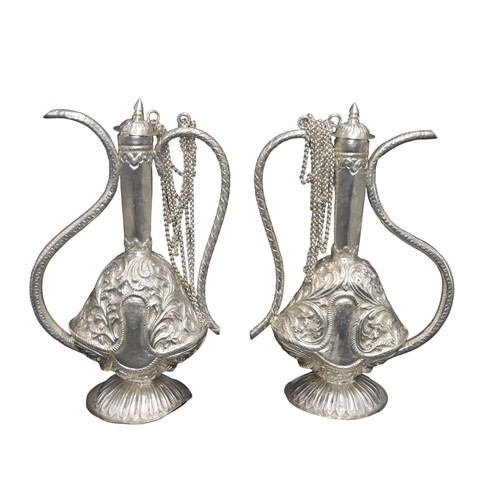 822 - A PAIR OF PERSIAN STYLE SILVER EWERS, elegant scrolling handles and spout, the body with scroll foli... 