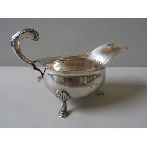 589 - A GEORGIAN SILVER SAUCE BOAT, with indented rim, ornate 'C' scroll foliate handle, raised on three s... 