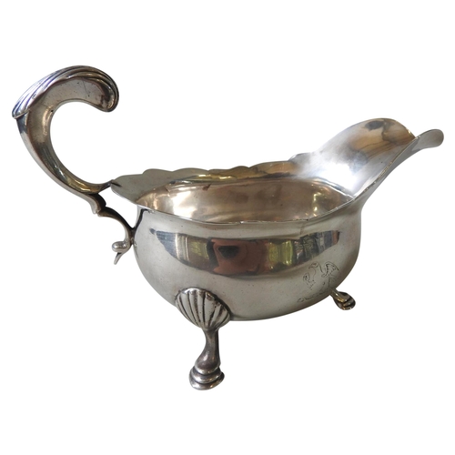 589 - A GEORGIAN SILVER SAUCE BOAT, with indented rim, ornate 'C' scroll foliate handle, raised on three s... 