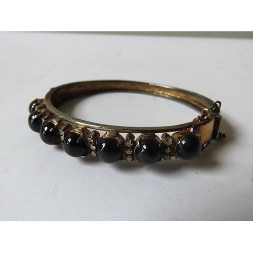 538 - A BLACK DIOPSIDE BANGLE, set with seven circular cabochon-cut stones showing star effect, each space... 