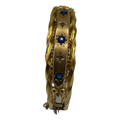 562 - A LATE VICTORIAN 9CT GOLD HOLLOW HINGED BANGLE, CIRCA 1880set with three circular-cut sapphires and ... 