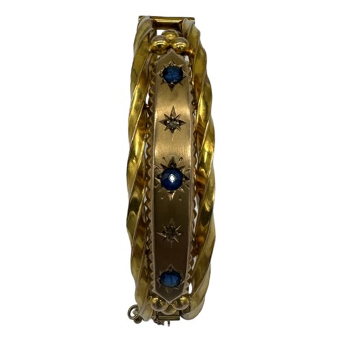 562 - A LATE VICTORIAN 9CT GOLD HOLLOW HINGED BANGLE, CIRCA 1880set with three circular-cut sapphires and ... 