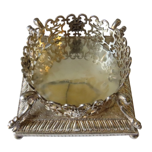 699 - AN ORNATE GEORGE II SILVER BOTTLE STAND, a pierced circular lattice gallery adorned with Neo Classic... 