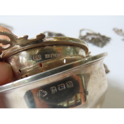 660 - FIVE SILVER DECANTER LABELS, TEA STRAINER AND CUP, including a group of three chased vine leaf form ... 