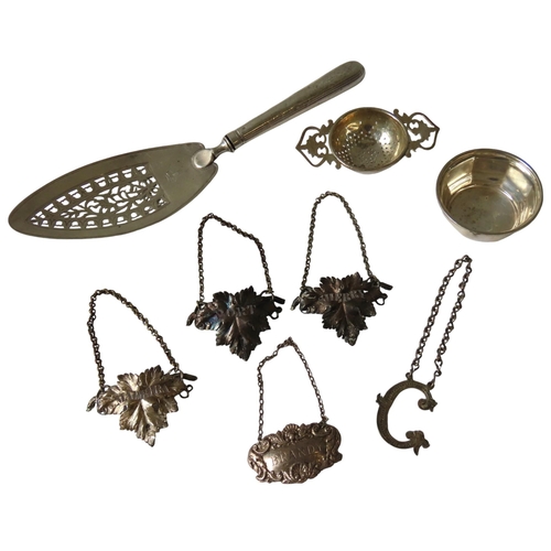 660 - FIVE SILVER DECANTER LABELS, TEA STRAINER AND CUP, including a group of three chased vine leaf form ... 