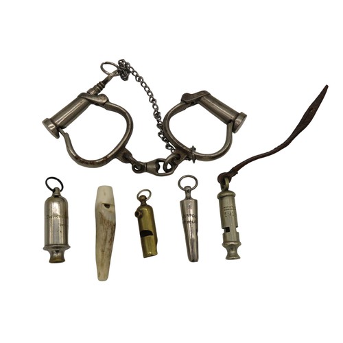 565 - A PAIR OF VINTAGE IRON HANDCUFFS TOGETHER WITH FIVE WHISTLES, including a Liverpool Police Whistle, ... 